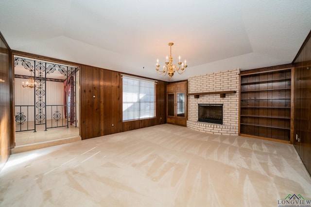 unfurnished living room with an inviting chandelier, a raised ceiling, wooden walls, built in shelves, and a fireplace