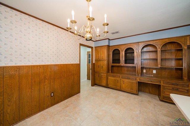 unfurnished office with a chandelier, wooden walls, crown molding, and built in desk