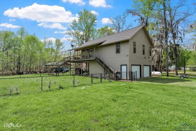 rear view of property featuring a yard, a garage, and a deck