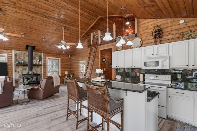 kitchen with white appliances, a wood stove, backsplash, a kitchen breakfast bar, and white cabinetry