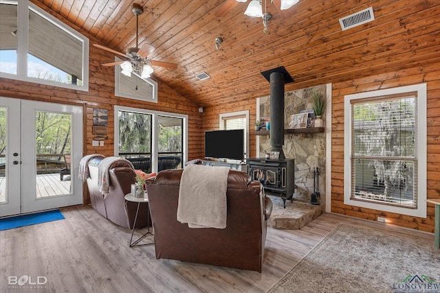 living room featuring french doors, high vaulted ceiling, a wood stove, and rustic walls