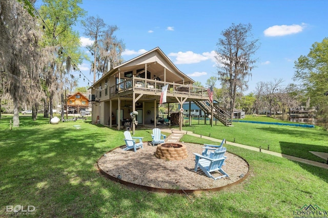 rear view of property with a deck with water view, a yard, and an outdoor fire pit