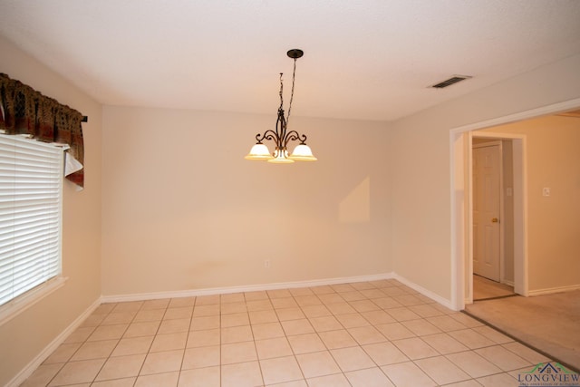 tiled spare room featuring an inviting chandelier