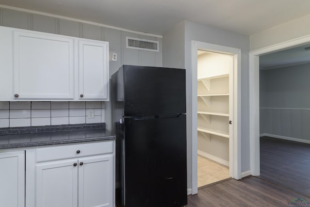 kitchen with white cabinets, hardwood / wood-style flooring, and black fridge