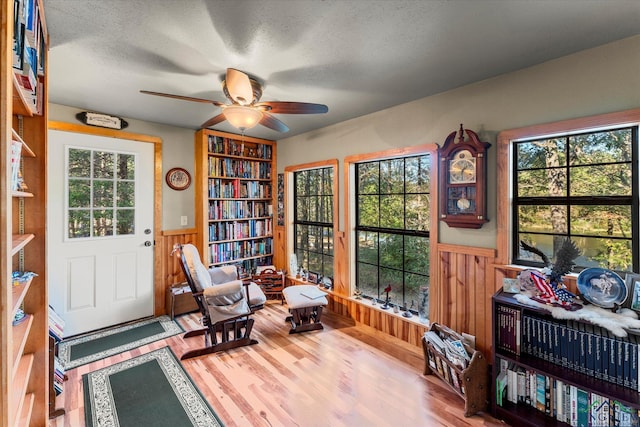 sitting room with hardwood / wood-style flooring, ceiling fan, a textured ceiling, and wooden walls