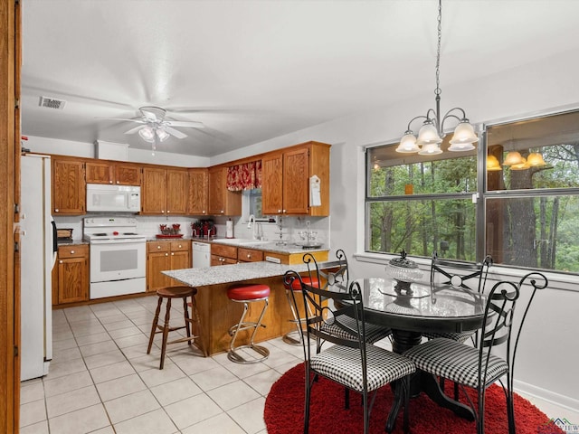 kitchen with hanging light fixtures, tasteful backsplash, kitchen peninsula, white appliances, and a kitchen bar