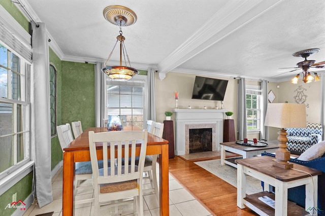 dining space featuring a fireplace with flush hearth, tile patterned floors, ornamental molding, and ceiling fan