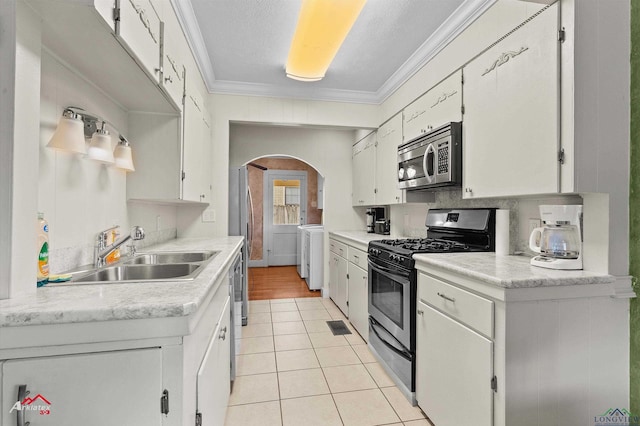kitchen featuring arched walkways, a sink, separate washer and dryer, stainless steel appliances, and light tile patterned flooring