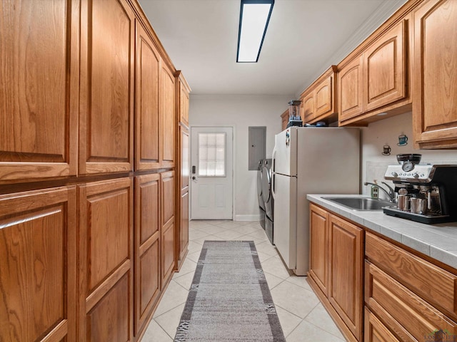 kitchen featuring sink, washing machine and dryer, white refrigerator, light tile patterned flooring, and tile countertops