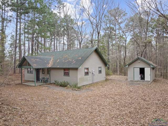 exterior space with a shingled roof, a patio, and an outbuilding