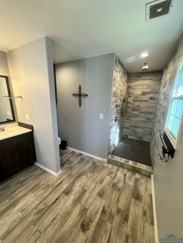 bathroom featuring vanity, wood-type flooring, toilet, and tiled shower