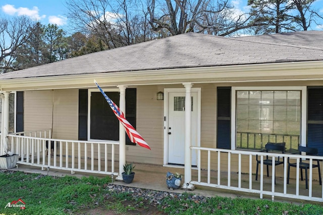 view of exterior entry featuring a shingled roof and a porch