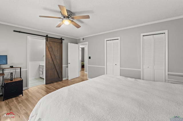 bedroom with ornamental molding, wood finished floors, two closets, and a barn door