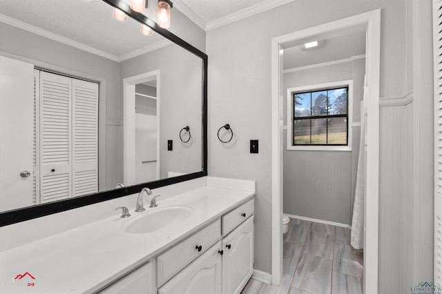 bathroom with baseboards, toilet, crown molding, vanity, and a closet