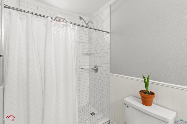 bathroom featuring a textured wall, toilet, a wainscoted wall, a stall shower, and crown molding