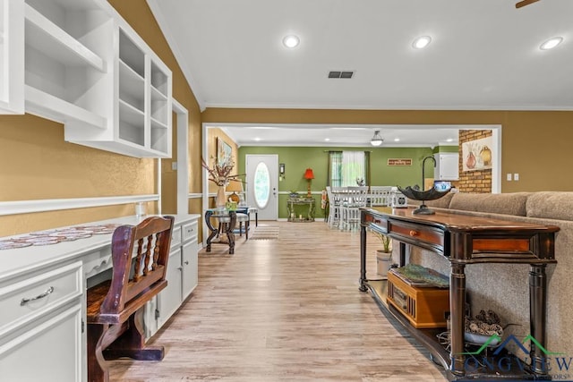 interior space with crown molding, white cabinets, built in desk, light wood finished floors, and visible vents