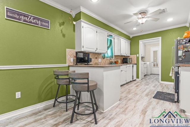 kitchen featuring a kitchen breakfast bar, tasteful backsplash, white cabinets, light wood-style flooring, and washer and clothes dryer