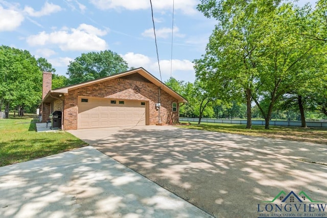 view of front facade featuring a chimney, a front yard, a garage, brick siding, and concrete driveway