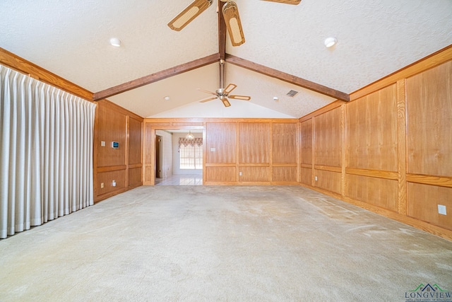 empty room featuring carpet flooring, a textured ceiling, ceiling fan, wooden walls, and lofted ceiling with beams