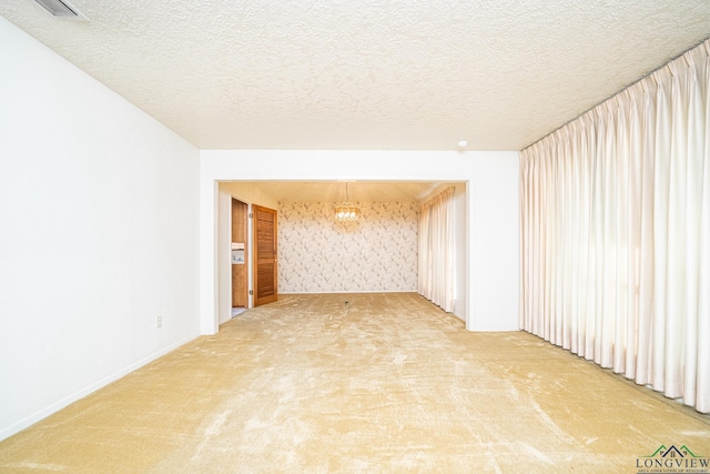 carpeted empty room with a textured ceiling and an inviting chandelier