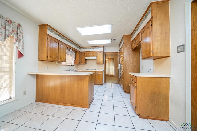 kitchen with kitchen peninsula, sink, light tile patterned floors, and a textured ceiling