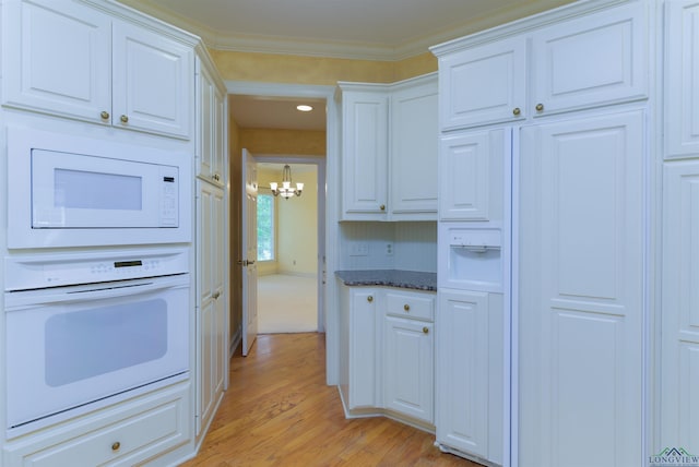 kitchen with white appliances, an inviting chandelier, dark stone countertops, white cabinets, and light hardwood / wood-style floors