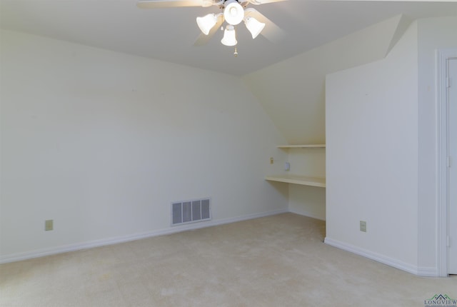 empty room featuring ceiling fan, vaulted ceiling, light colored carpet, and built in shelves