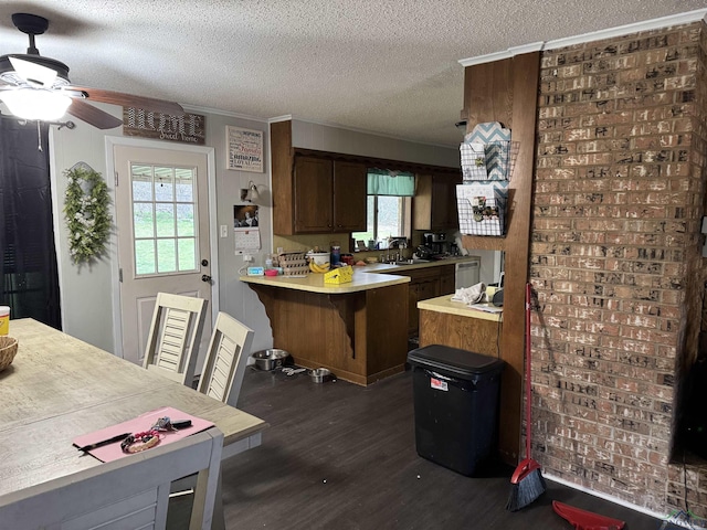 kitchen featuring a textured ceiling, a peninsula, a breakfast bar, dark wood-type flooring, and light countertops