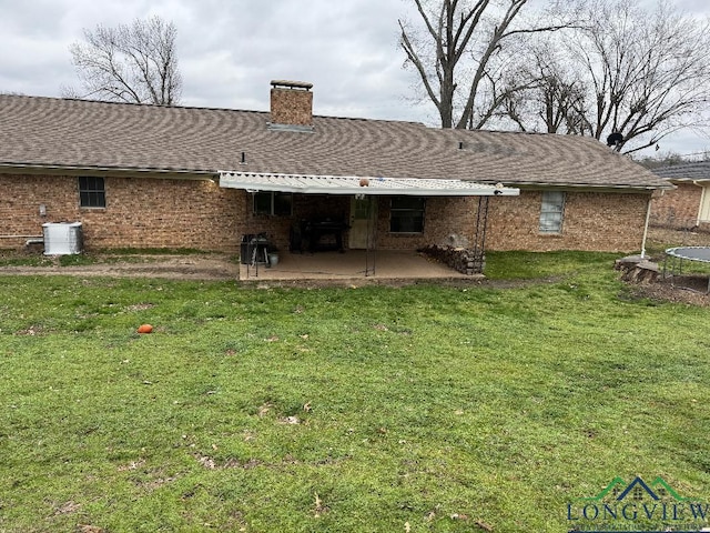 rear view of property featuring a patio, a yard, a shingled roof, and brick siding