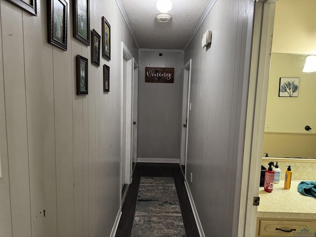 hallway with a textured ceiling, ornamental molding, and baseboards