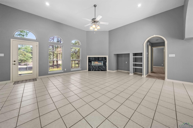 1804 W Lake Dr, Gladewater, TX 75647 - unfurnished living room with ceiling fan, light tile patterned floors, a fireplace, a towering ceiling, and a healthy amount of sunlight