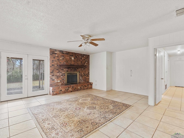 unfurnished living room with ceiling fan, french doors, a brick fireplace, a textured ceiling, and light tile patterned floors