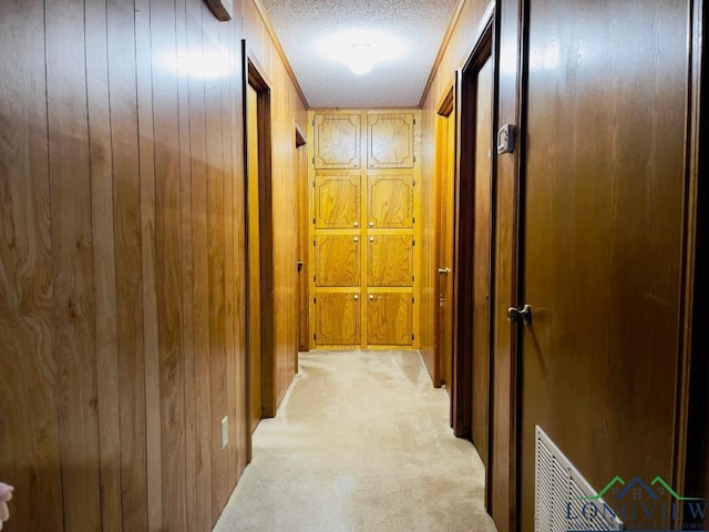 hallway with light carpet, a textured ceiling, crown molding, and wooden walls