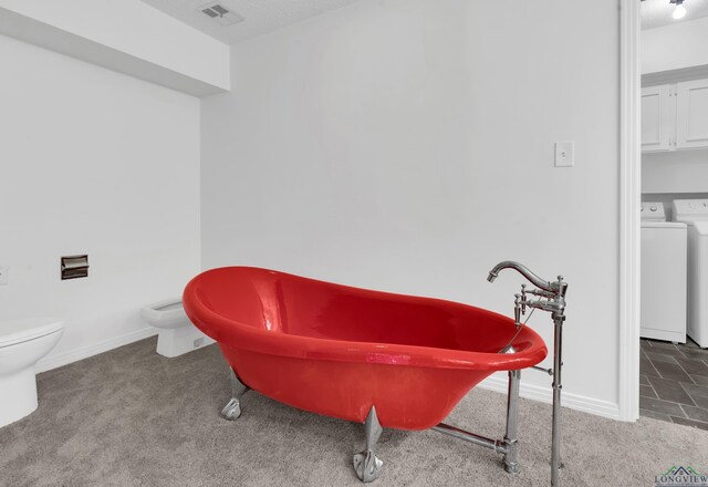 bathroom with a bathtub, toilet, and separate washer and dryer