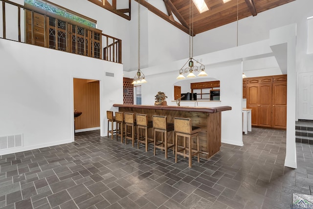 kitchen featuring a breakfast bar, wooden ceiling, high vaulted ceiling, decorative light fixtures, and kitchen peninsula