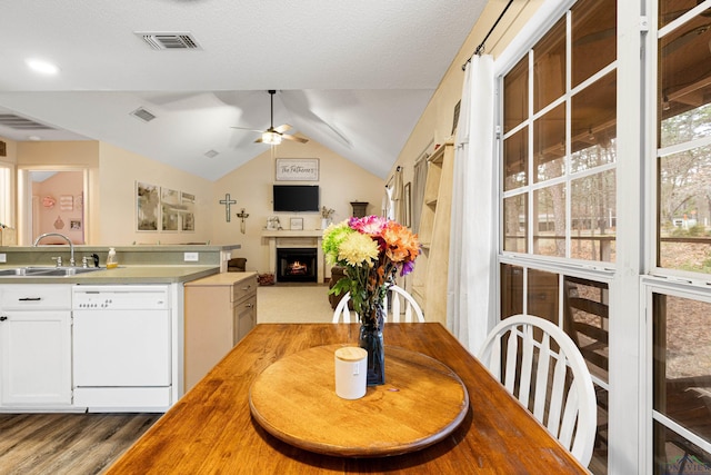 kitchen with lofted ceiling, visible vents, white dishwasher, a sink, and a lit fireplace