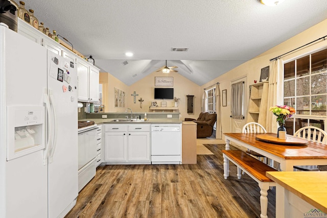 kitchen featuring white appliances, dark wood-style flooring, a peninsula, vaulted ceiling, and a sink