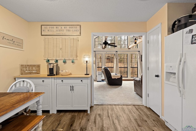 kitchen featuring a textured ceiling, white fridge with ice dispenser, a ceiling fan, and wood finished floors