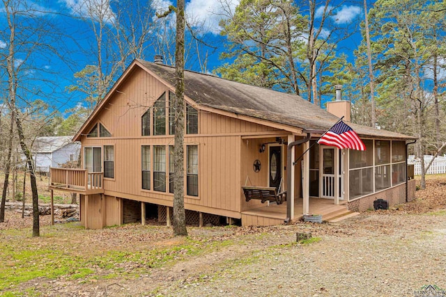 rear view of property featuring a shingled roof, a chimney, a wooden deck, and a sunroom