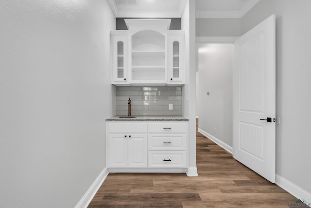 bar featuring wood finished floors, a sink, decorative backsplash, baseboards, and ornamental molding
