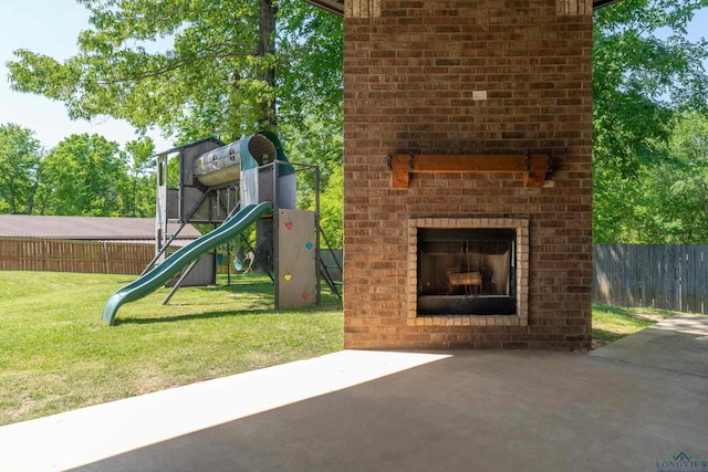 view of playground featuring fence, a yard, an outdoor brick fireplace, and a patio