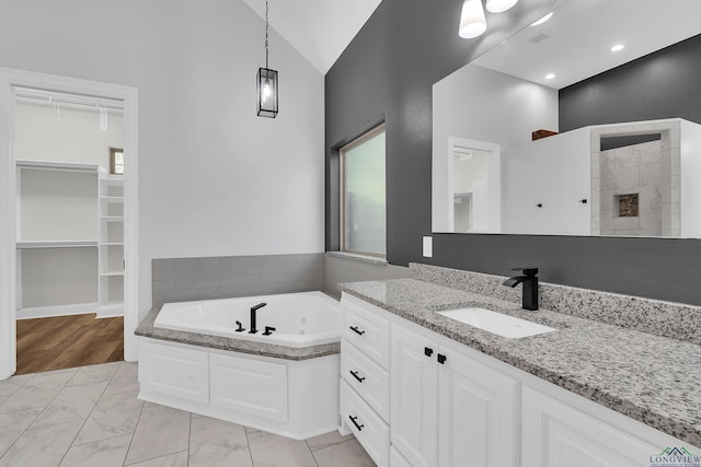 bathroom with vaulted ceiling, a spacious closet, marble finish floor, a tile fireplace, and a jetted tub