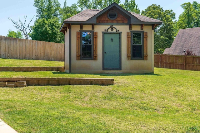 exterior space with a fenced backyard, a front lawn, an outbuilding, and a shingled roof