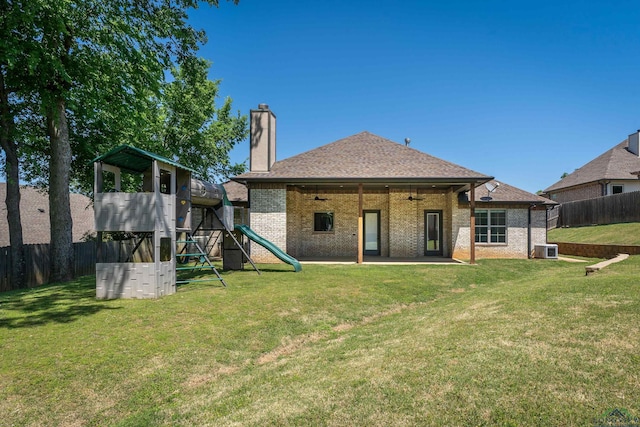 rear view of house featuring a playground, fence, brick siding, a ceiling fan, and a yard