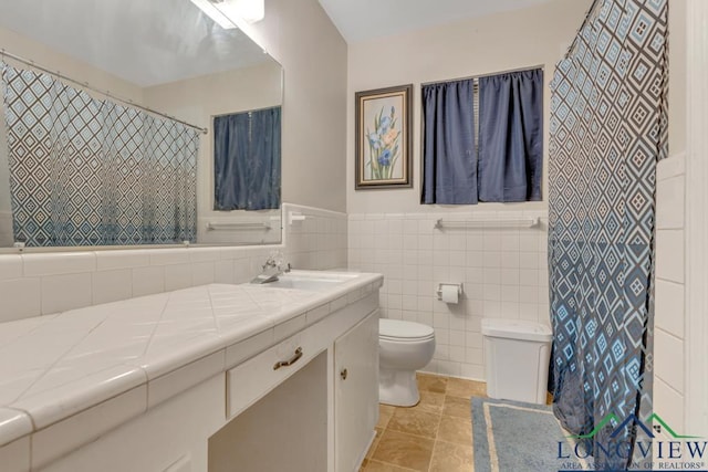 bathroom with vanity, toilet, and tile walls