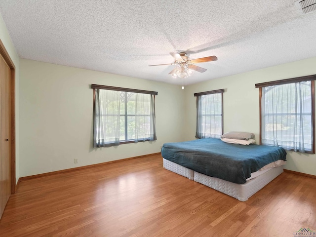 bedroom with multiple windows, wood-type flooring, a closet, and ceiling fan