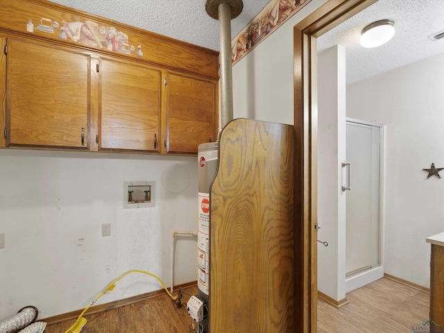 clothes washing area with cabinets, water heater, hookup for a washing machine, a textured ceiling, and light wood-type flooring