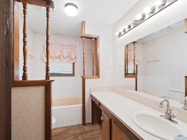 bathroom featuring vanity, a textured ceiling, hardwood / wood-style floors, tiled bath, and toilet