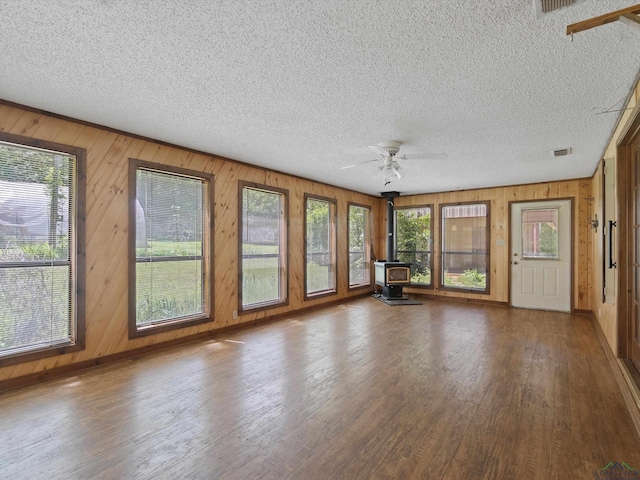 unfurnished sunroom with a wood stove and ceiling fan