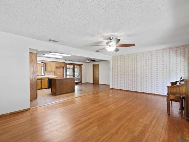 unfurnished living room with a textured ceiling, light hardwood / wood-style floors, and ceiling fan